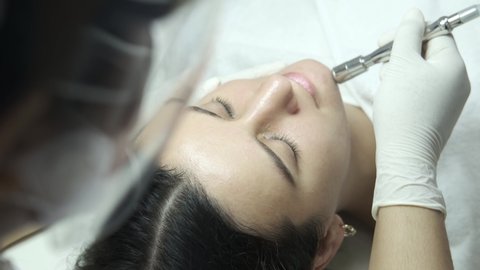 Young woman during microdermabrasion treatment in beauty salon. Professional cosmetologit performing diamond exfoliation and peeling procedure on female client face. Healthcare and wellness