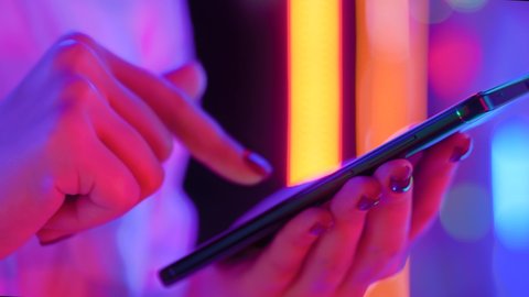 Woman using smartphone device at interactive exhibition or museum with purple illumination - scrolling and touching - close up side view. Futuristic, retrowave, immersive, entertainment concept