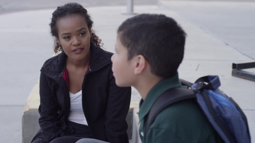 Female mentor listens to student after school outside school building
