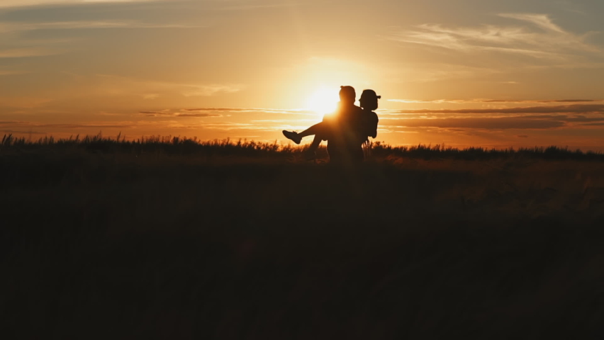 Silhouette of couple in golden field and beautiful sunset. Young and romantic family enjoying. Man hold woman in arms with love on summer evening. People talking and hugging by heart. Two person.