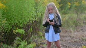 Cute little blonde girl using mobile apps outdoors. Concept of gaming and children	