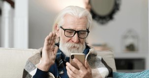 Close up portrait of Caucasian old man in glasses sitting in room and video chatting on cellphone. Ill senior male in warm plaid speaking on online video call on smartphone at home. Talk concept
