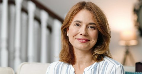 Close up of pretty cheerful woman in good mood sitting indoors. Joyful beautiful Caucasian middle-aged female with happy face smiling to camera at home. Positive emotions. Portrait concept