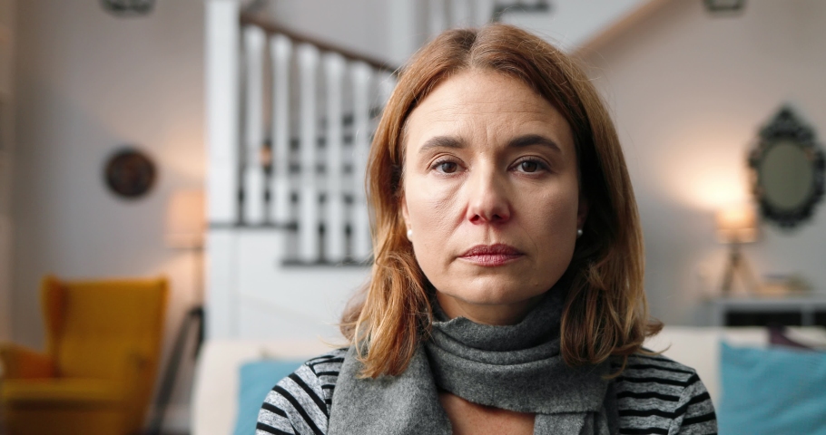 Close up of beautiful unwell middle-aged woman with serious sad face sitting in room at home and looking at camera. Portrait of Caucasian sick female in warm scarf isolated indoor. Virus concept | Shutterstock HD Video #1061350543
