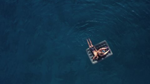 Zenith timelapse of a couple of unrecognizable bathers on an inflatable mattress swimming in the blue sea of Salento, Puglia / Italy