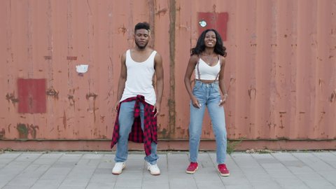 Street Dancing. Young Couple Dancing On The Street. Black Guy And Girl Move Rhythmically. They Make The Same Movements. Young People In Jeans. They Dance Modern Dances. Stylish Girl With Long Hair And
