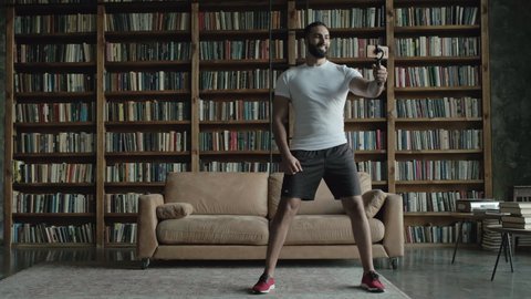 Nice Guy From The Middle East Squats. Many Books On The Shelves And Chairs In The Room. He Shoots Himself On The Phone.