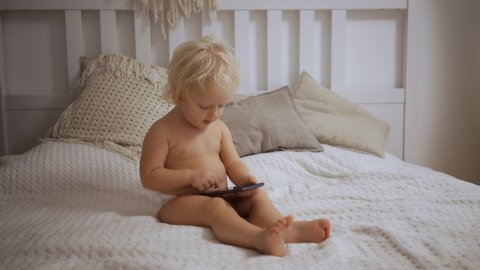 A portrait of a cute baby checking smartphone lying in a bed