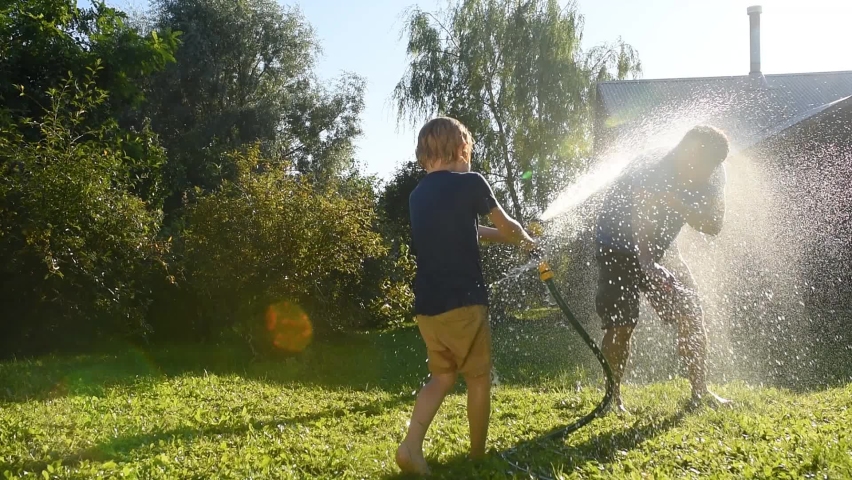 Funny little boy with his father playing with garden hose in sunny backyard. Preschooler child having fun with spray of water. Summer outdoor activity for family with kids. Royalty-Free Stock Footage #1061351782