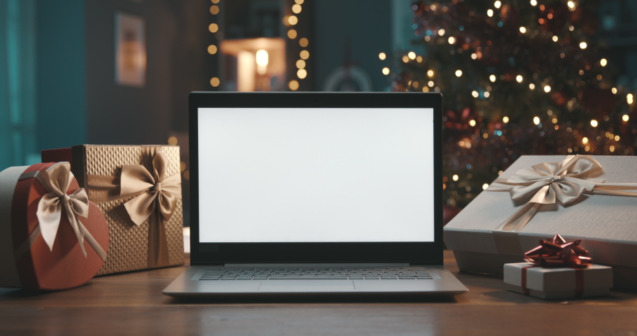 Laptop with blank screen on a desktop at home, Christmas gifts and decorated tree in the background Royalty-Free Stock Footage #1061354437