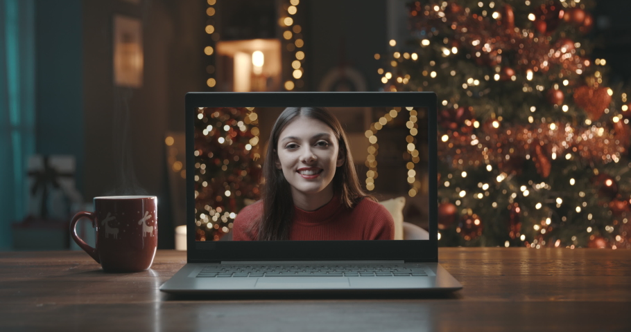 Smiling woman on a videocall, she is happy and wishing a merry Christmas online, Christmas tree and decorated room interior in the background Royalty-Free Stock Footage #1061354446