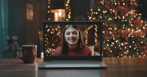 Smiling woman on a videocall, she is happy and wishing a merry Christmas online, Christmas tree and decorated room interior in the background