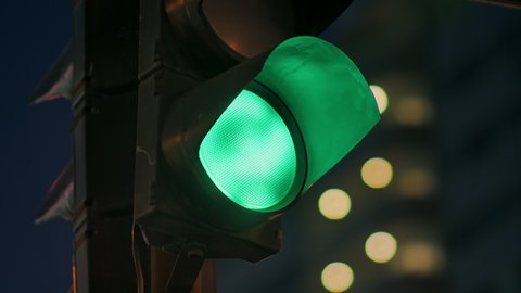 Traffic light against the background of the evening city flashes green and changes to orange.