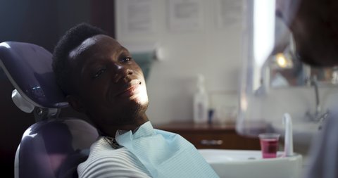 Cheerful African American teenage boy talking to professional dentist while sitting in chair during check up