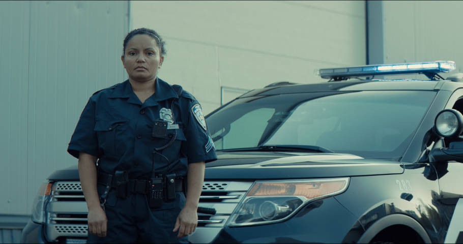 Mixed race female police officer posing against police car with flashing lights. Shot on RED cinema camera with 2x Anamorphic lens Royalty-Free Stock Footage #1061365837