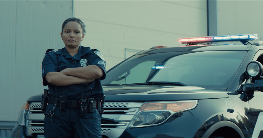 Mixed race female police officer posing against police car with flashing lights. Shot on RED cinema camera with 2x Anamorphic lens | Shutterstock HD Video #1061365837