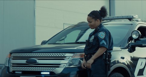 Mixed race female police officer posing against police car with flashing lights. Shot on RED cinema camera with 2x Anamorphic lens