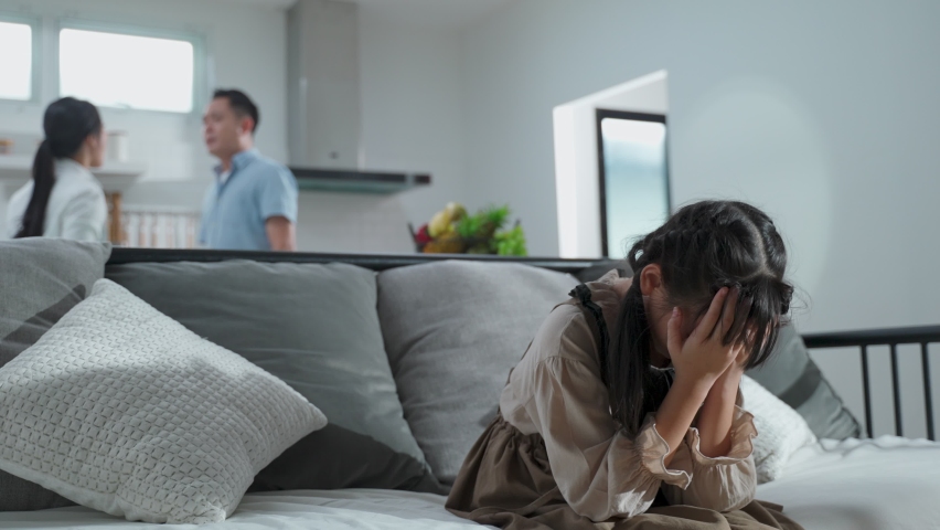Asian girl kid sitting and crying on bed while parents having fighting or quarrel conflict at home. Child covering face and eyes with hands do not want to see the violence. Domestic problem in family. | Shutterstock HD Video #1061365891