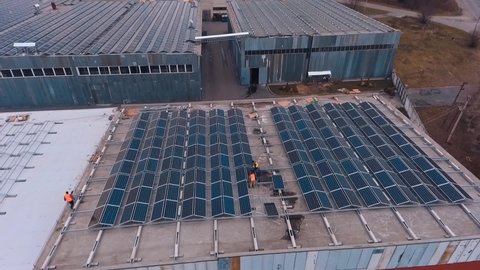 Installing solar panels on the foof of plant or factory. Additional source of electricity. Green energy. Video from the top.