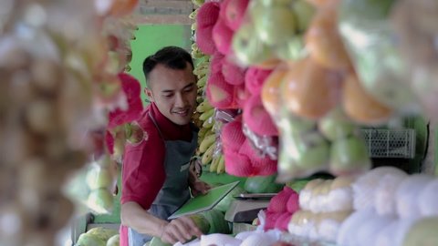 a male shop owner holding a digital tablet while observing fresh fruit in a fruit shop