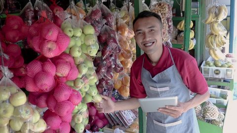 a male shop owner holding a digital tablet while observing fresh fruit in a fruit shop