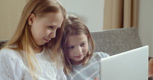 Two cute little preschool children friends girl laughing watching online cartoons video movie together, happy kids sisters learn use laptop computer sit on sofa at home, children technology concept