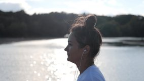 Young pretty woman in headphones runs on the beach, the sun glare from the water. Concept healthy running lifestyle, sport and outdoor exercise
