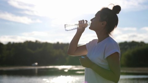 Girl quench their thirst on a hot sunny day after a jog, drink water. Healthy lifestyle.Woman in the Open air Drinks Water from a Bottle