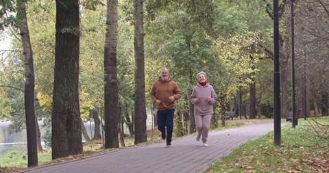 Wellness, adult couple running around a forest Park, autumn day, gray-haired man and woman plays sports in a city Park, aerobic exercise, autumn mood.