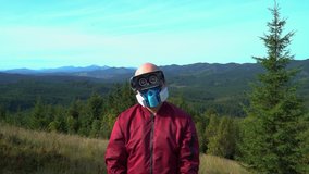 Young hairless man standing in the mountains in vr virtual reality glasses technologies and face mask respirator ffp protection infection against air pollution