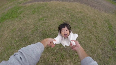 Running asian toddler girl comes and dad hands holding spinning little happy smiling cute daughter playing together at playground in residential area POV shot carefree family enjoying weekend relaxing