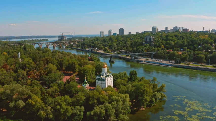 Aerial view over beautiful white church on island surrounding by river - while sunset. Overflight  above old church on a green island with river. Ukraine, Dnepr city. 2020 year.