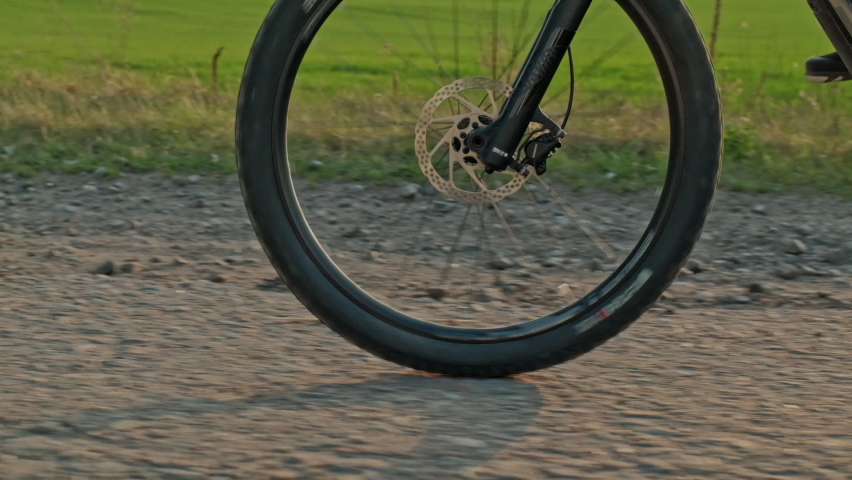 Close-up of a Bicycle wheel driving on gravel. Slow motion of  cyclist pedaling the pedals on the bike. Tracking shot of bike wheel moving.  Men's feet turn the pedals of a mountain bike. Bike tire  Royalty-Free Stock Footage #1061386801