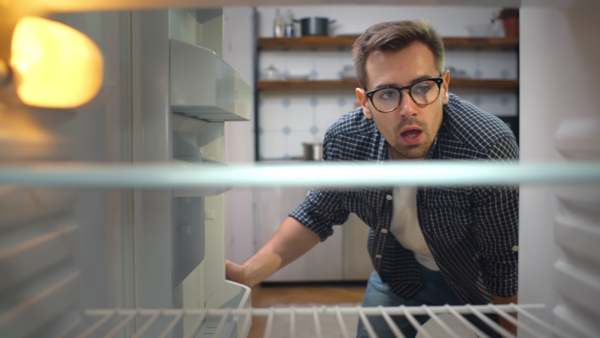 Hungry young man looking for food in an empty fridge. View from inside of hipster guy in glasses opening refrigerator finding no food feeling sad and disappointed. | Shutterstock HD Video #1061388715