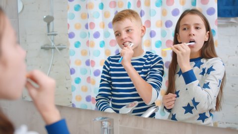 Cute brother and sister kids in pajama brushing teeth looking into bathroom mirror. Reflection of boy and girl standing in bathroom in morning doing routine