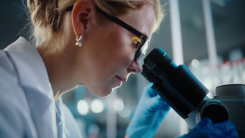 In Bright Medical Science Laboratory: Beautiful Microbiologist Wearing Glasses Looks Under Microscope Analyzing Sample. Brilliant Scientist, working with High-Tech Equipment. Low Angle Close-up Shot | Shutterstock HD Video #1061389426