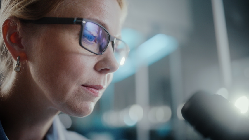 In Bright Medical Science Laboratory: Beautiful Microbiologist Wearing Glasses Looks Under Microscope Analyzing Sample. Brilliant Scientist, working with High-Tech Equipment. Macro Close-up Shot Royalty-Free Stock Footage #1061389429