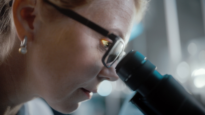 In Bright Medical Science Laboratory: Beautiful Microbiologist Wearing Glasses Looks Under Microscope Analyzing Sample. Brilliant Scientist, working with High-Tech Equipment. Macro Close-up Shot | Shutterstock HD Video #1061389432