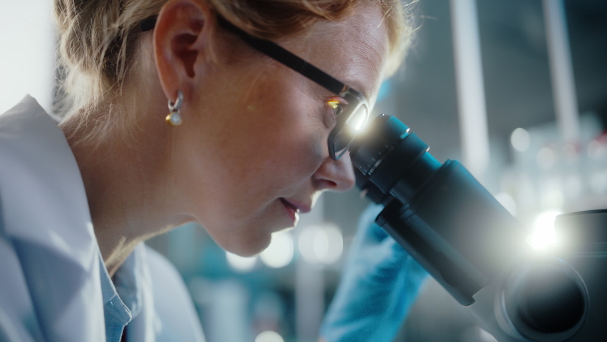 In Bright Medical Science Laboratory: Beautiful Microbiologist Wearing Glasses Looks Under Microscope Analyzing Sample. Brilliant Scientist working with High-Tech Equipment. Close-up Shot | Shutterstock HD Video #1061389435