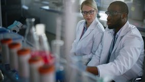 Bright Medical Science Laboratory with Diverse Team of Research Scientists Working. Microbiologist Looks Under Microscope Talks to Biochemist Using Laptop. High-Tech Equipment. Slow Motion Dolly Shot - Powered by Shutterstock - Get 15% off with code: PIKWIZARD15