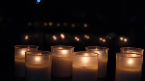 many candles mysteriously burn in front of the window in complete darkness, blurred reflections and lights of lamps in the glass, the concept of religion, faith, mourning for the dead