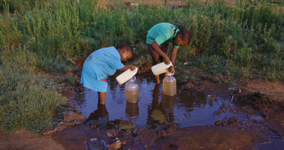 Water crisis. Poverty. Inequality.Drought.Close-up of two young black African boys collecting dirty unsafe drinking water for domestic use.  Poor living conditions and no access to clean running water Royalty-Free Stock Footage #1061394247