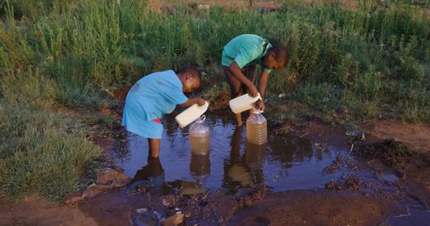 Water crisis. Poverty. Inequality.Drought.Close-up of two young black African boys collecting dirty unsafe drinking water for domestic use.  Poor living conditions and no access to clean running water