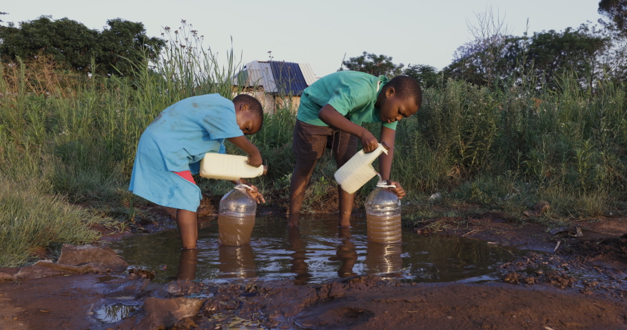 Poverty.Inequality.Water crisis. Close-up of two young black African boys collecting dirty unsafe drinking water for domestic use.  Poor living conditions and no access to clean running water Royalty-Free Stock Footage #1061394250