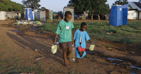 Water crisis. poverty. Inequality.Drought.Two young black African boys carrying home dirty unsafe drinking water for domestic use.  Poor living conditions and no access to clean running water
