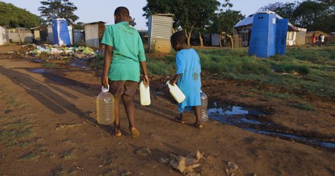 Water crisis and poverty. Two young black African boys carrying home dirty unsafe drinking water for domestic use.  Poor living conditions and no access to clean running water