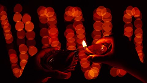 Woman holding and illuminating diya or oil clay lamp, close up shot in a decorative,lit, festive background. Indian hindu festival Diwali celebration at night.