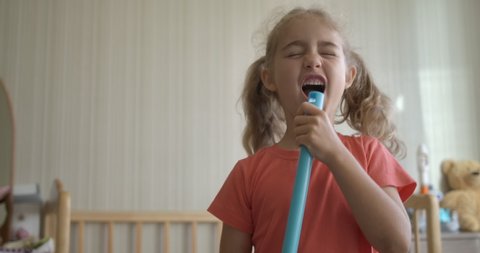 Little Fun Creative Girl Singing and Using Broom Handle as Microphone. Child Using Mop as Microphone While Singing in Domestic Room. Enjoying Spring Cleaning. Playful Creative Kid Dancing With Mop.