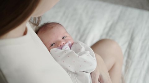 Portrait of a newborn baby in the arms of the mother. A young woman holds her lovely child in her arms and looks at her. Over the shoulder shot