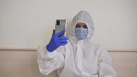A female doctor in a protective suit makes a video call on a smartphone